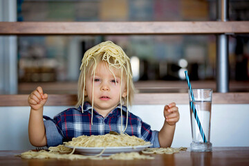Little baby boy, toddler child, eating spaghetti for lunch and making feeding teddy bear friend