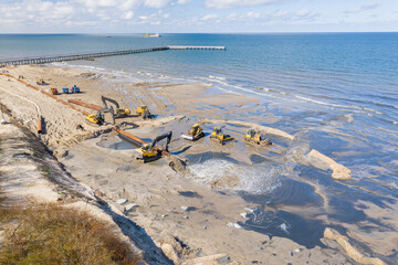 Beach restoration sand Bulldozers. Mud flows from the pipe with excavator behind for the...