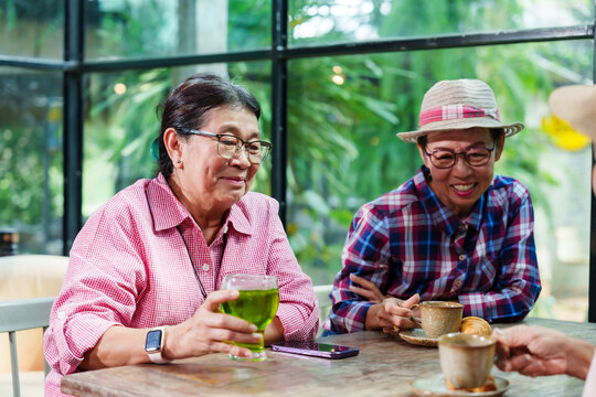 Senior Asian woman with close friend after retirement enjoying hot beverage at cafe. Elderly friends sipping coffee, sharing meaningful conversation, and cherishing time together. Warm and happy