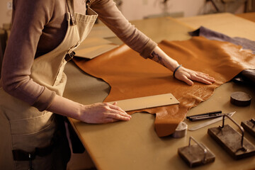 Hands cutting leather on workbench with precision, surrounded by tools, suggesting craftsmanship in...