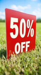 Bright Red Sale Sign Displaying Fifty Percent Discount in a Green Field Under Clear Blue Sky