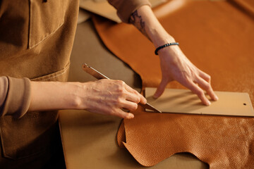 Close-up of hands skillfully cutting leather with a blade, showing detailed craftsmanship. Table covered with pieces of leather and tools for crafting
