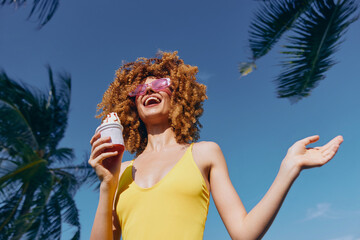 Happy young woman enjoying ice cream in summer sunshine with palm trees in the background