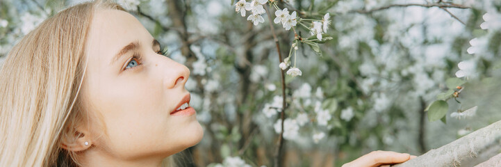 Blonde girl on a spring walk in the garden with cherry blossoms. Female portrait, close-up. A girl in a pink polka dot dress.