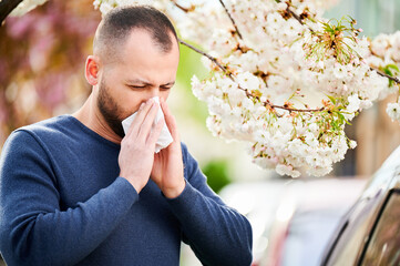 Man allergic suffering from seasonal allergy at spring in blossoming garden at springtime. Man...