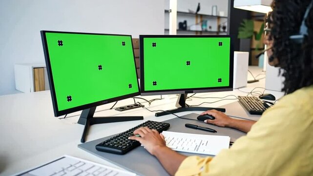 A women working on two monitors with a green screen and tracking markers for VFX work, suitable for chroma keying green screen footage.