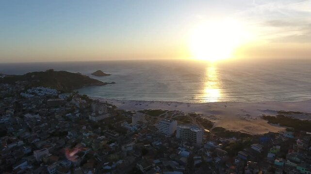 Imagens a&eacute;reas deslumbrantes capturam o p&ocirc;r do sol na praia de Arraial do Cabo, transformando o c&eacute;u em uma paleta de cores vibrantes, com tons de laranja, rosa e dourado refletindo nas &aacute;guas cristalin