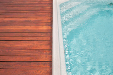 Clear blue water meets polished wooden deck at a serene outdoor pool area on a sunny day