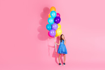 Young girl holding colorful balloons in front of pink wall, cheerful and playful moment