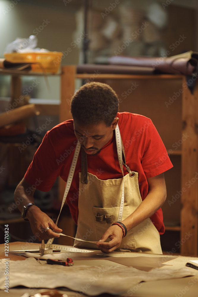 Poster tailor measuring fabric for precise cuts surrounded by tools and materials in workshop. focus on han