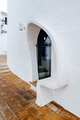 This image captures a charming architectural detail of a whitewashed building in Menorca, featuring a unique curved doorway design. Ideal for showcasing traditional Mediterranean architecture