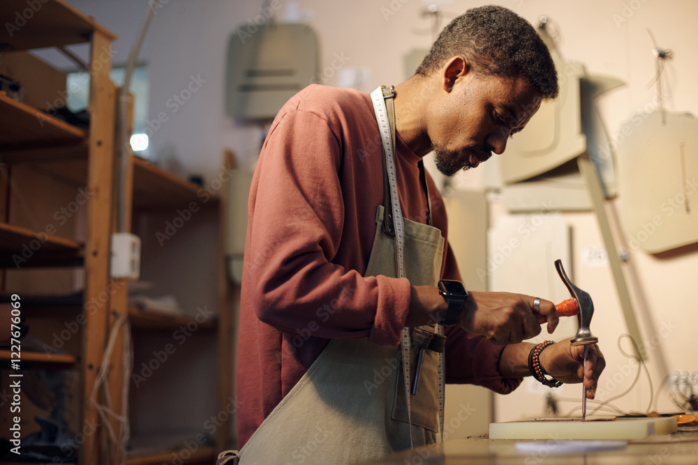 Poster person focused on woodworking task in a well-equipped studio with various tools hanging on walls. ca