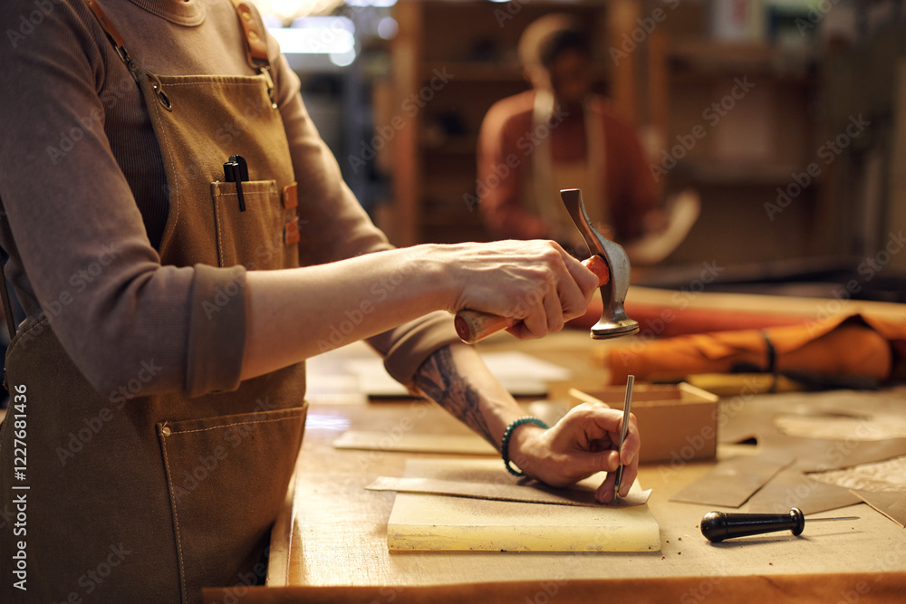 Poster artisan meticulously crafting leather goods in workshop environment holding chisel and hammer for pr