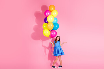 Girl in blue dress holding colorful balloons on bright pink background, expressing joy and vibrance