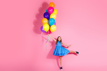 Playful young girl in blue dress holding colorful balloons against a vibrant pink background