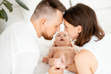 mom, dad with a baby, an international family, a Caucasian mom with an Asian husband and a baby in her arms in the bedroom gently hugs the baby holding in her arms, a place for text