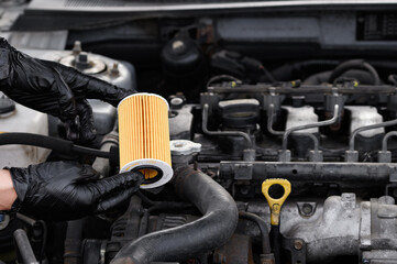 Auto mechanic holds paper oil filter for diesel cars against background of engine compartment of car. Concept of timely replacement of auto parts, replacement of oil and oil filter of car.