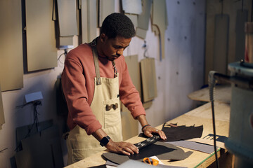 Professional leatherworker meticulously cutting leather pieces using a specialized tool in...
