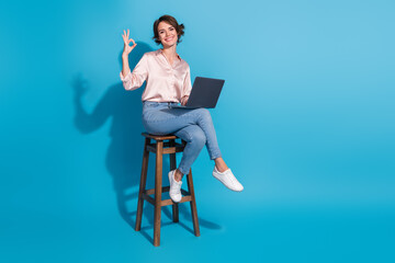 Confident young woman gesturing OK while working on laptop in stylish attire