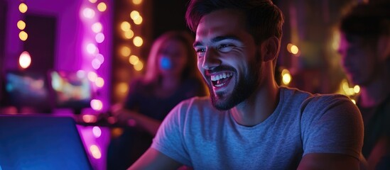 Fototapeta premium Cheerful young man immersed in online gaming with friends during an exciting evening gathering at the gym filled with colorful lights and laughter