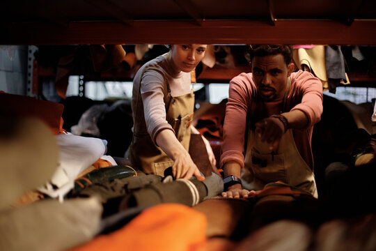 Two warehouse workers seen organizing and sorting various clothes on shelves, focused on their task. The ambient lighting provides a warm atmosphere, highlighting their concentration