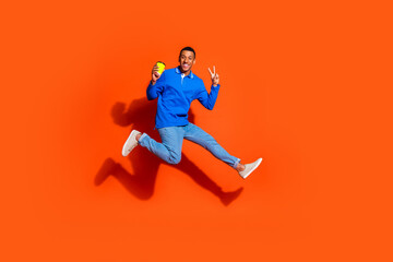 Young man jumping joyfully with playful expression against bright orange background