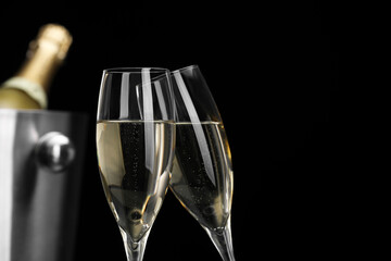 Champagne in glasses and ice bucket with bottle on black background, space for text