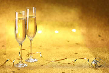 Champagne in glasses, confetti and streamers on golden background. Space for text