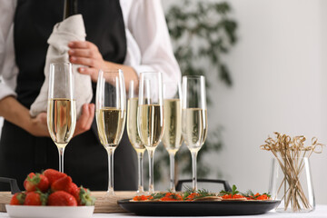 Waiter with bottle of drink, closeup. Champagne in glasses, strawberries and canapes on table