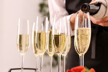 Waiter filling glasses with champagne indoors, closeup