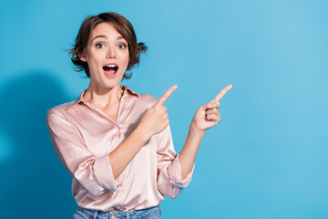 Young woman with a stylish bob points to the side on a blue background, dressed elegantly in a...