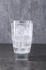Refreshing soda water with ice cubes in glass on grey table