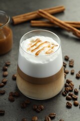Tasty latte macchiato in glass, coffee beans and cinnamon on grey table, closeup