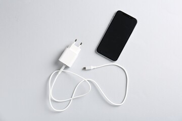USB power adapter with charge cable and smartphone on white background, flat lay