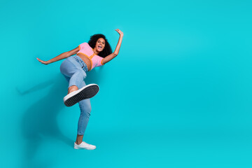 Fototapeta premium Cheerful young woman joyfully posing against a vibrant turquoise background