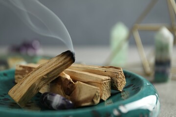Smoldering palo santo stick and gemstone on table, closeup