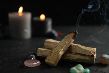 Smoldering palo santo stick, gemstones and burning candles on black table, closeup