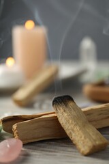 Smoldering palo santo stick and gemstone on wooden table, closeup