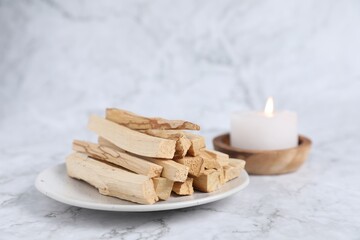 Palo santo sticks and burning candle on white marble table, closeup