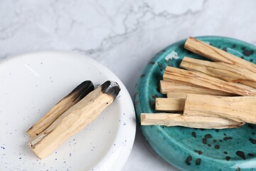 Whole and burnt palo santo sticks on white marble table, closeup