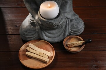 Palo santo sticks and statue with burning candle on wooden table, closeup