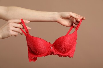 Woman holding red bra on dark beige background, closeup