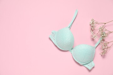 Beautiful turquoise bra and flowers on pale pink background, flat lay. Space for text