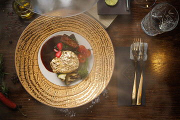 Gold-plated beef steak with grilled vegetables, cherry tomatoes, and a rich sauce. Gourmet dish garnished with edible flowers, served on an elegant plate in a fine dining restaurant