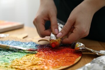 Woman squeezing paint from tube onto on palette at wooden table, closeup