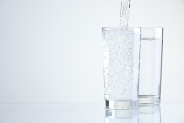 Pouring refreshing soda water into glasses on light background, closeup. Space for text