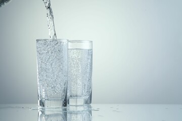 Pouring refreshing soda water into glasses on light grey background, closeup. Space for text