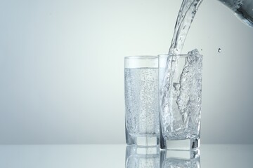 Pouring refreshing soda water into glasses on light grey background, closeup. Space for text