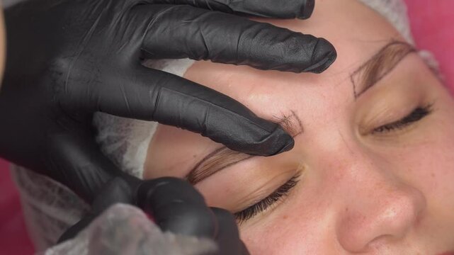 Makeup artist plucks eyebrows and doing eyebrow permanent makeup correction in a beauty salon. Concept makeup and cosmetology skin care.