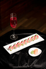 Pink tuna sushi served on a white plate with red wine, accompanied by wasabi and pickled ginger in white bowls, styled on black satin fabric with a warm brown background.